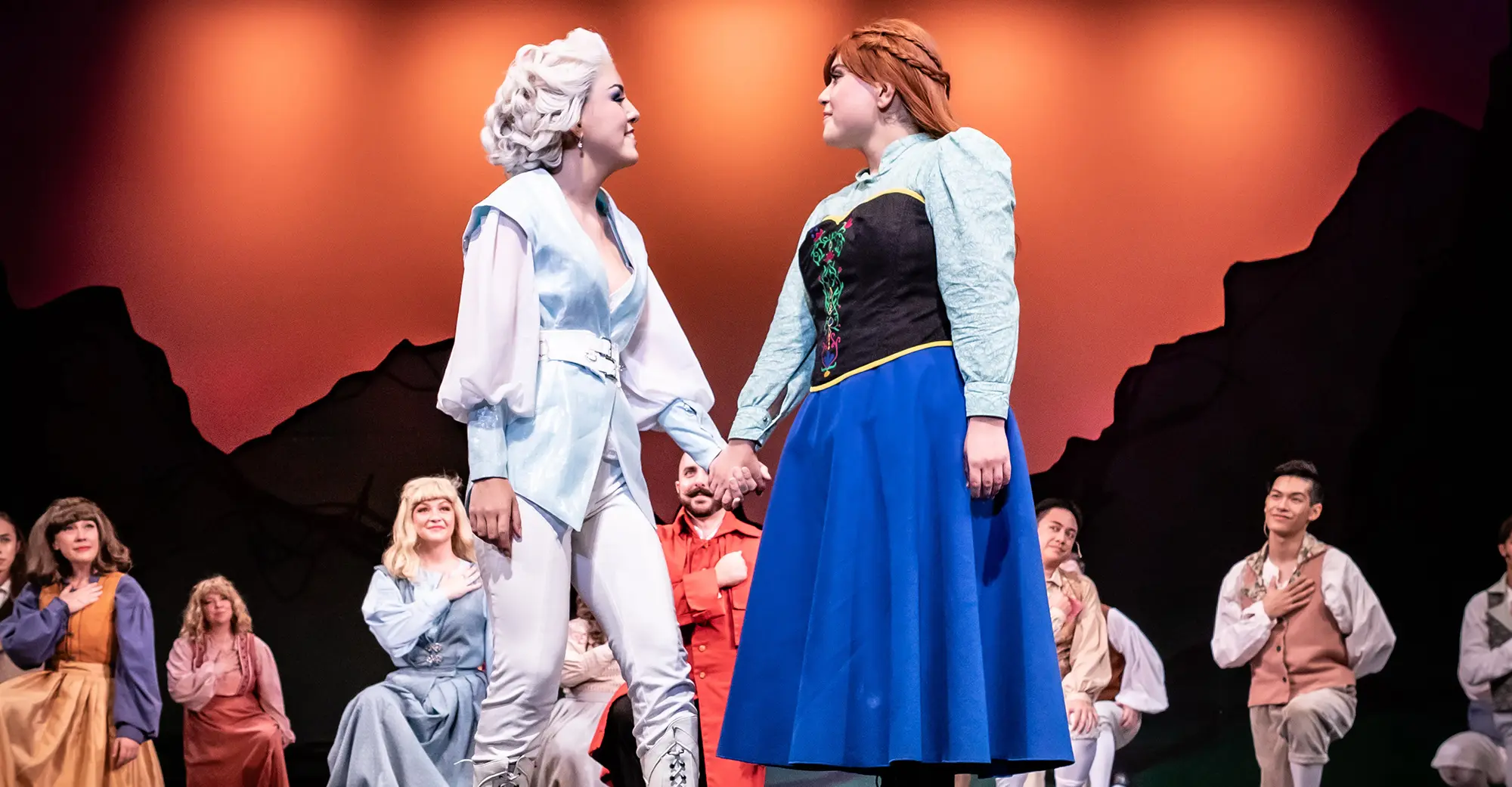 Frozen Anna and Esla characters hold hand on stage.